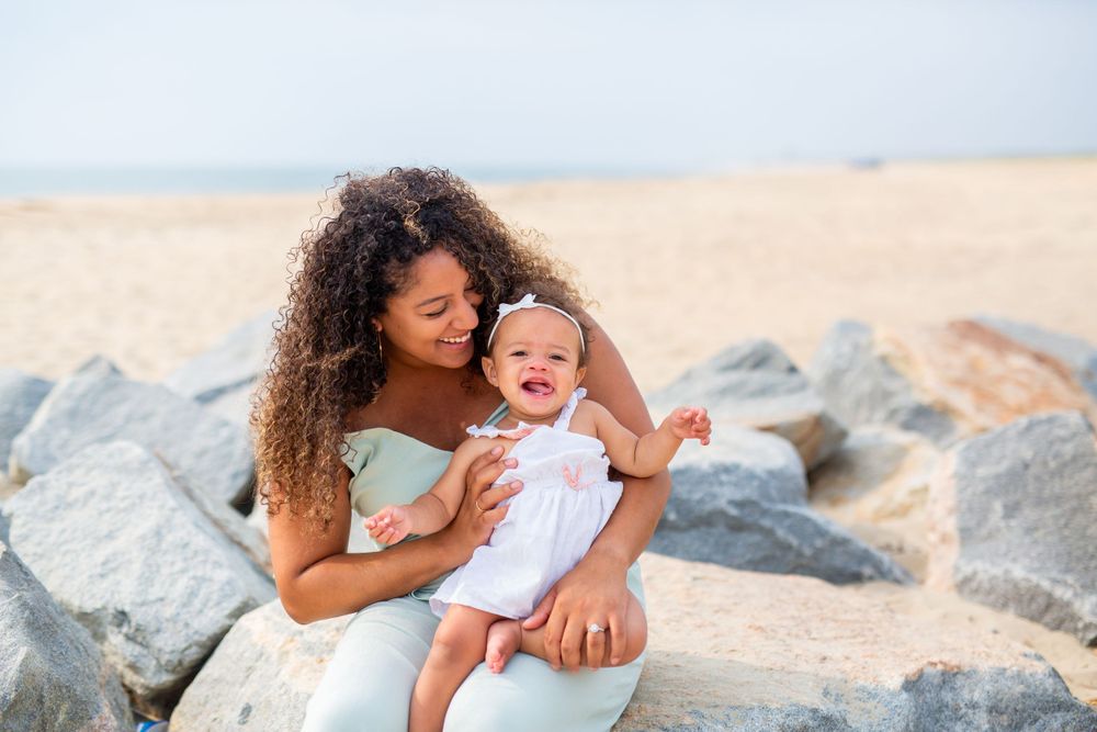 A parent and baby share a joyful moment together on a rocky beach.