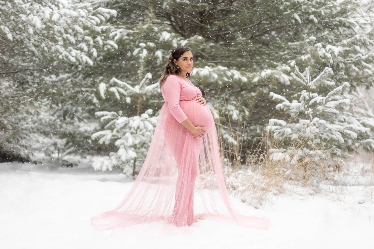 Girl in light pink dress holding her stomach during a winter maternity session