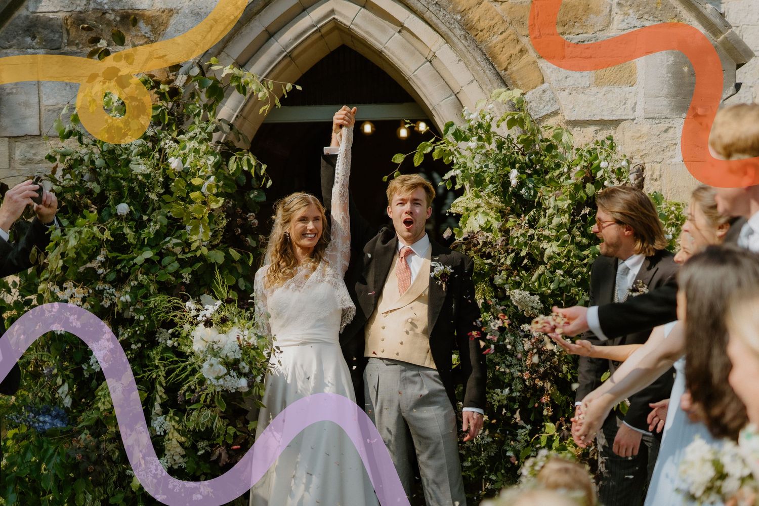 Newlyweds exit church under floral arch while guests throw confetti.