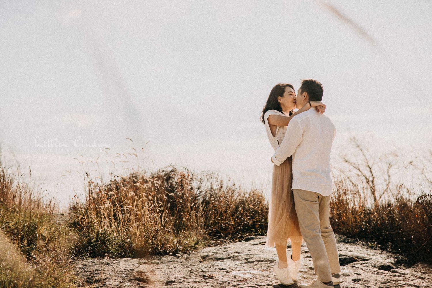 A romantic couple embraces on a hilltop during golden hour.
