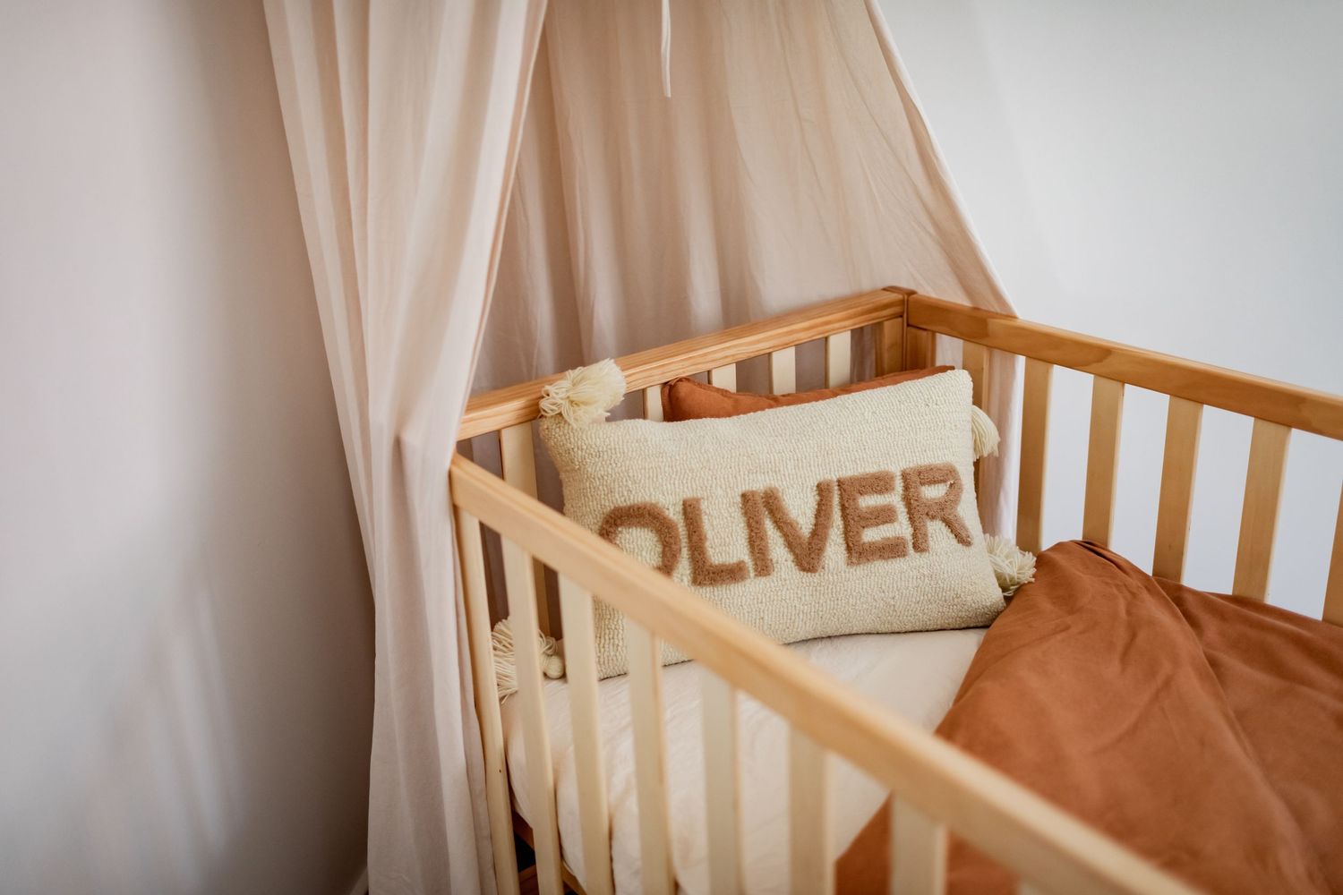 Wooden baby crib with cream canopy and personalized Oliver name pillow.