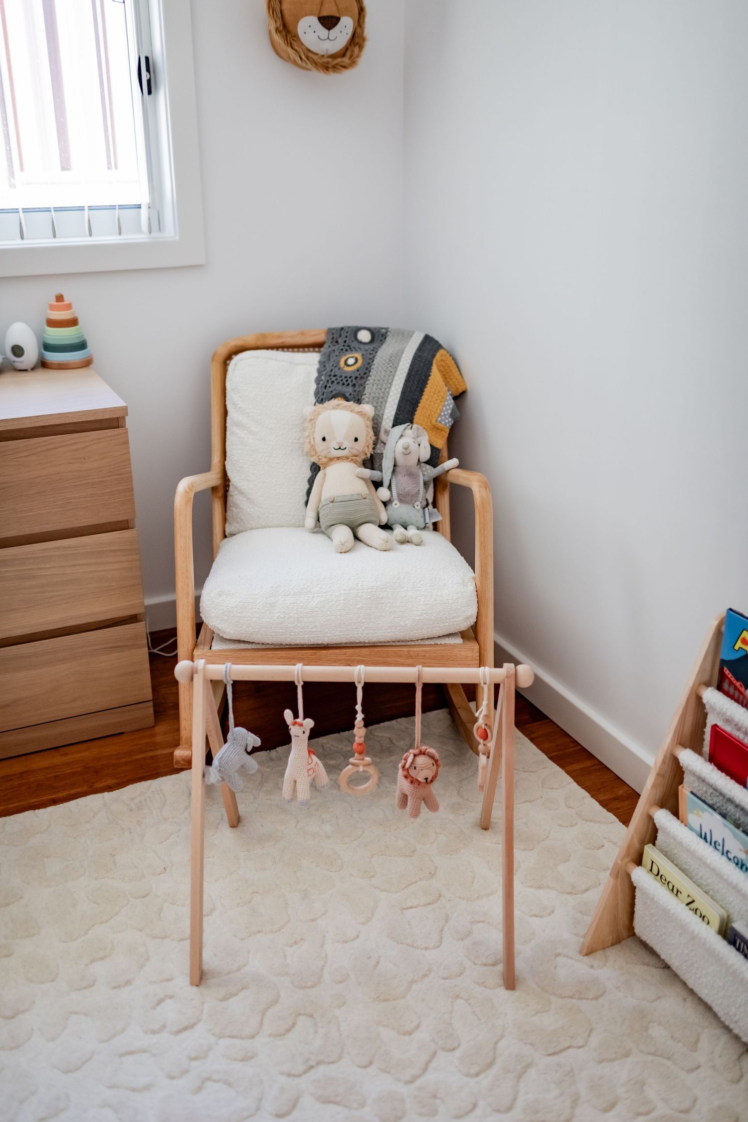 Cream cushioned wooden chair with hanging mobile toys in a cozy nursery corner.