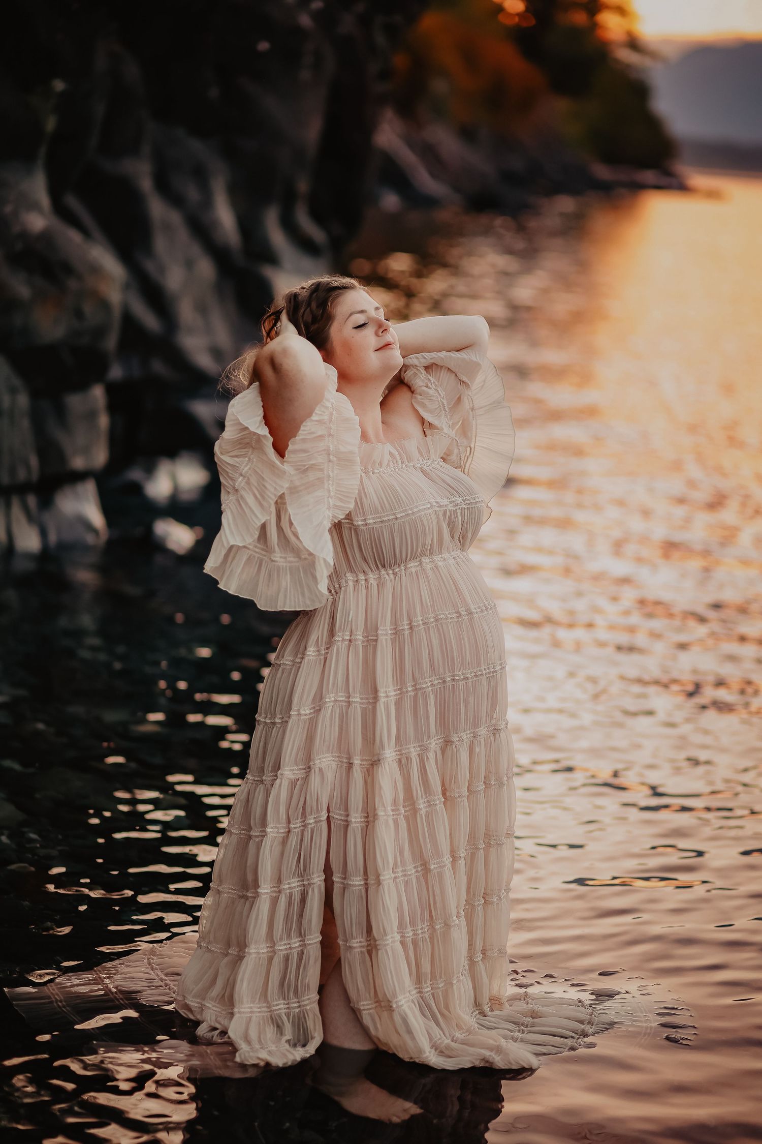 Romantic dress photography at sunset with water reflections and rocky backdrop.