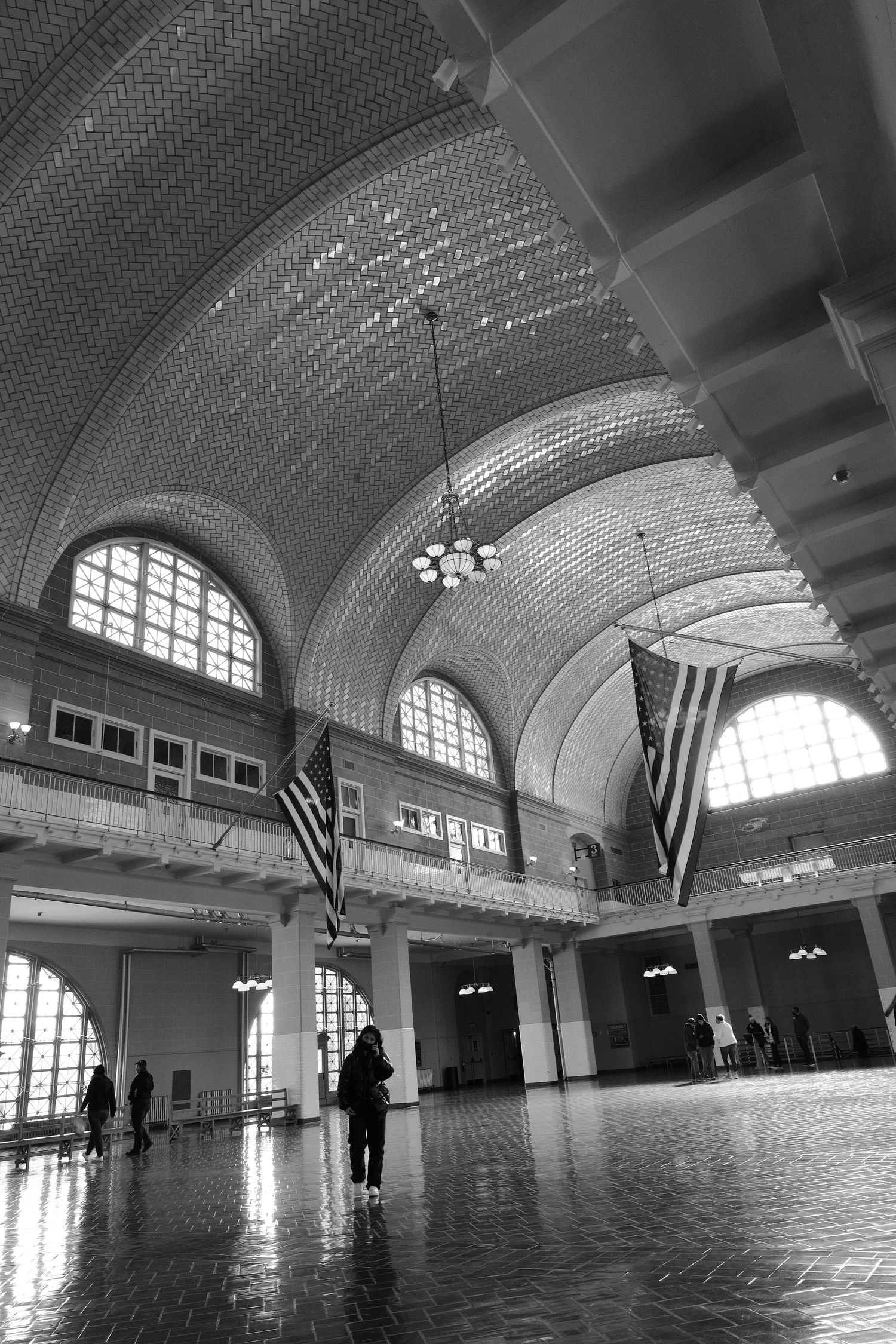Grand hall of Ellis Island with arched ceilings and American flags in black and white.