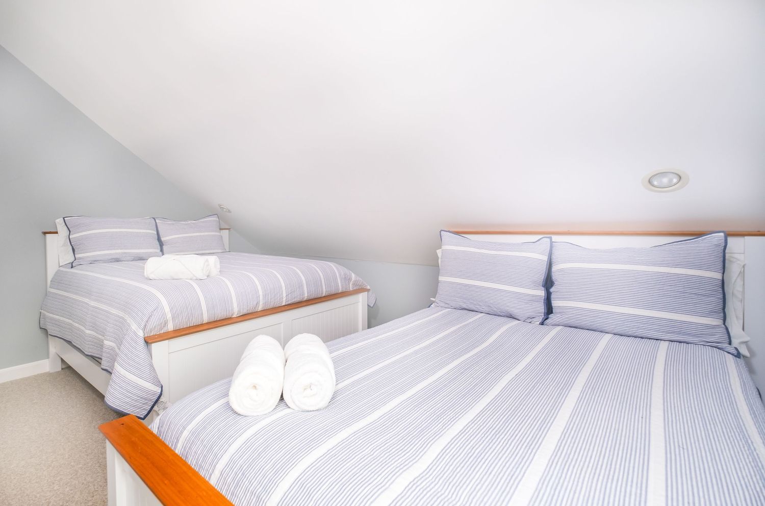 Attic bedroom with two beds dressed in striped bedding and white slippers on floor.