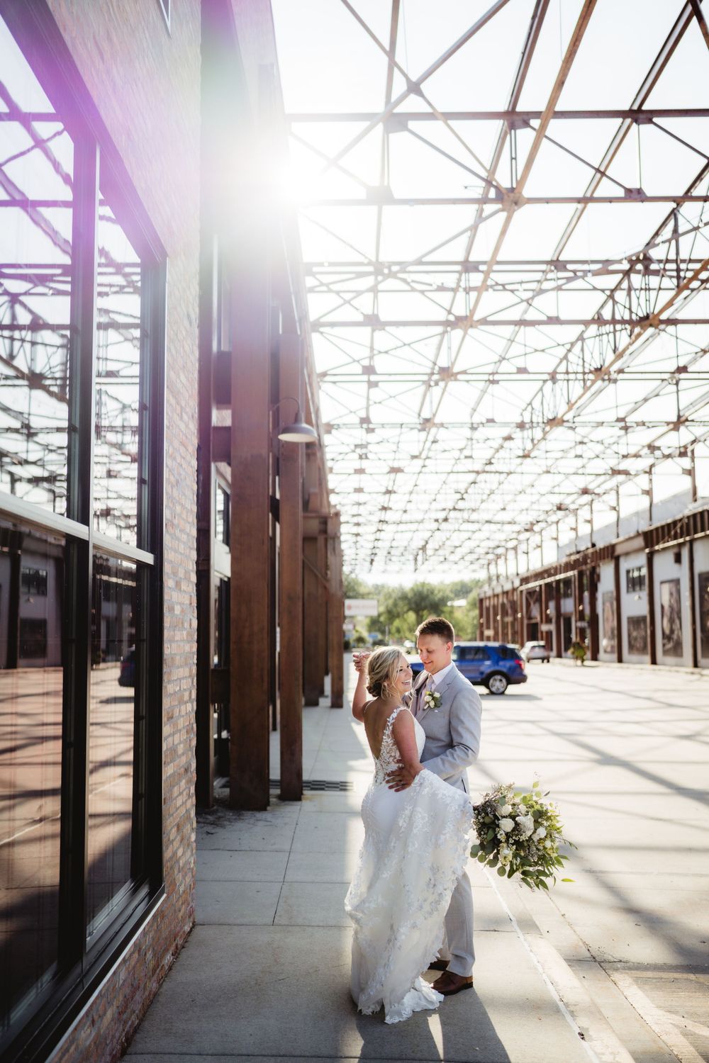 Romantic wedding portrait in sunlit industrial corridor with geometric ceiling.