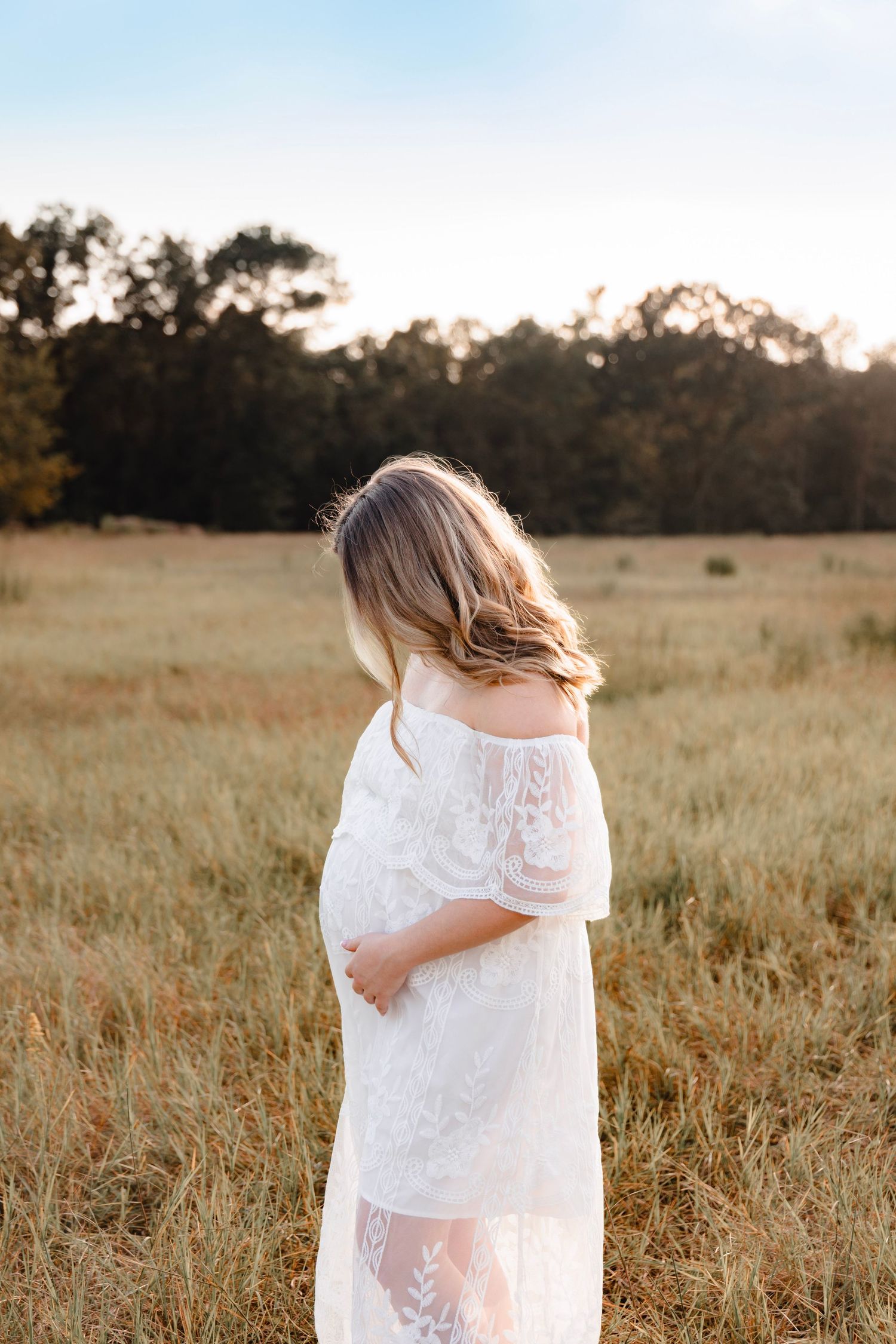 Woman in white lace dress twirling in golden field at sunset.