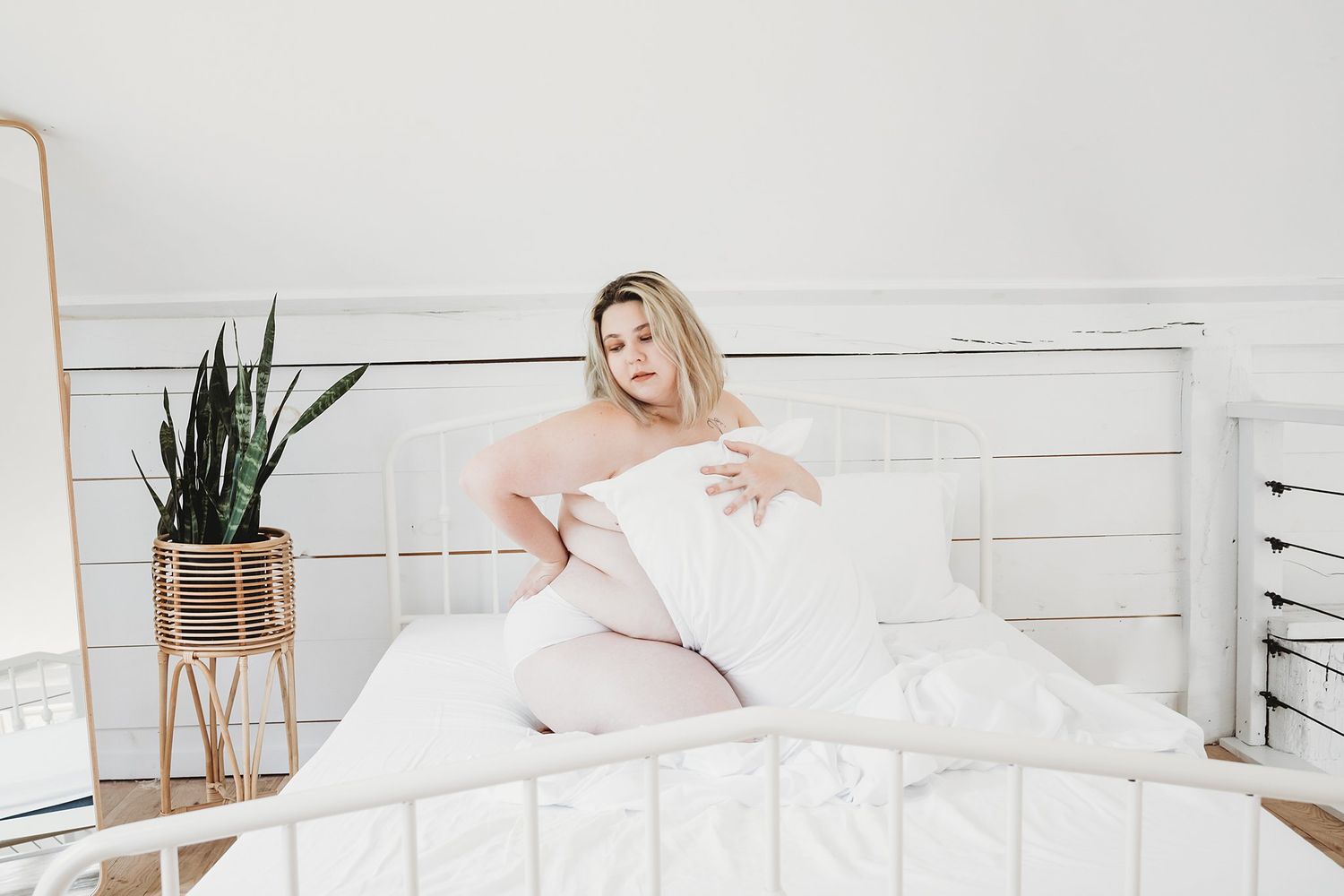 White minimalist bedroom with soft linens, plant decor, and bright natural lighting.