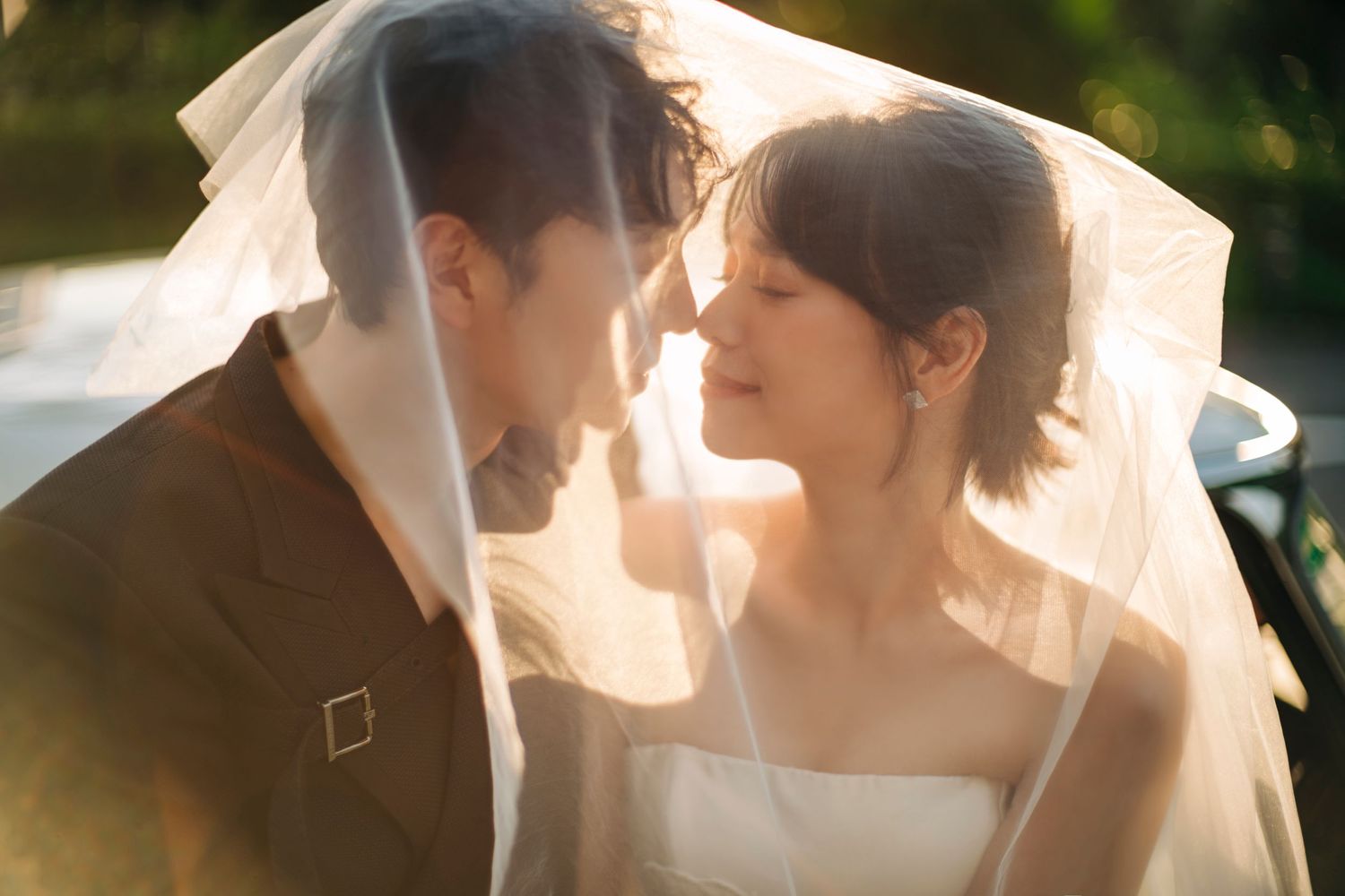 Romantic moment under a white veil during sunset wedding photoshoot.