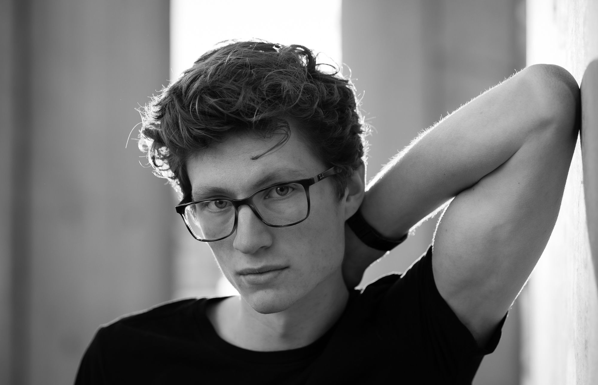 A man leans against a wall. A natural headshot. He wears a pair of nice glasses.