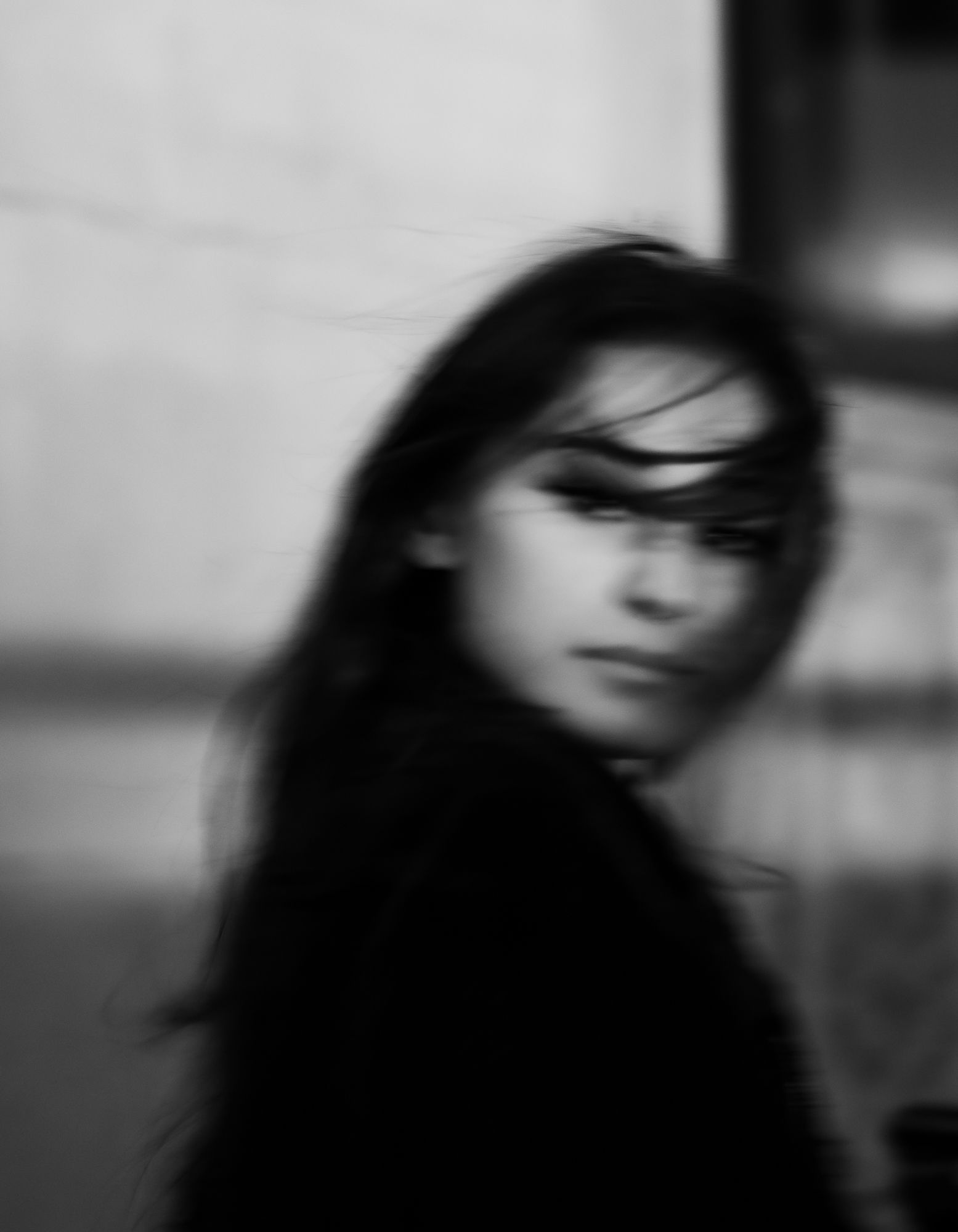 A woman looks over her shoulder to the camera as her hair blows across her face, covering her eyes.