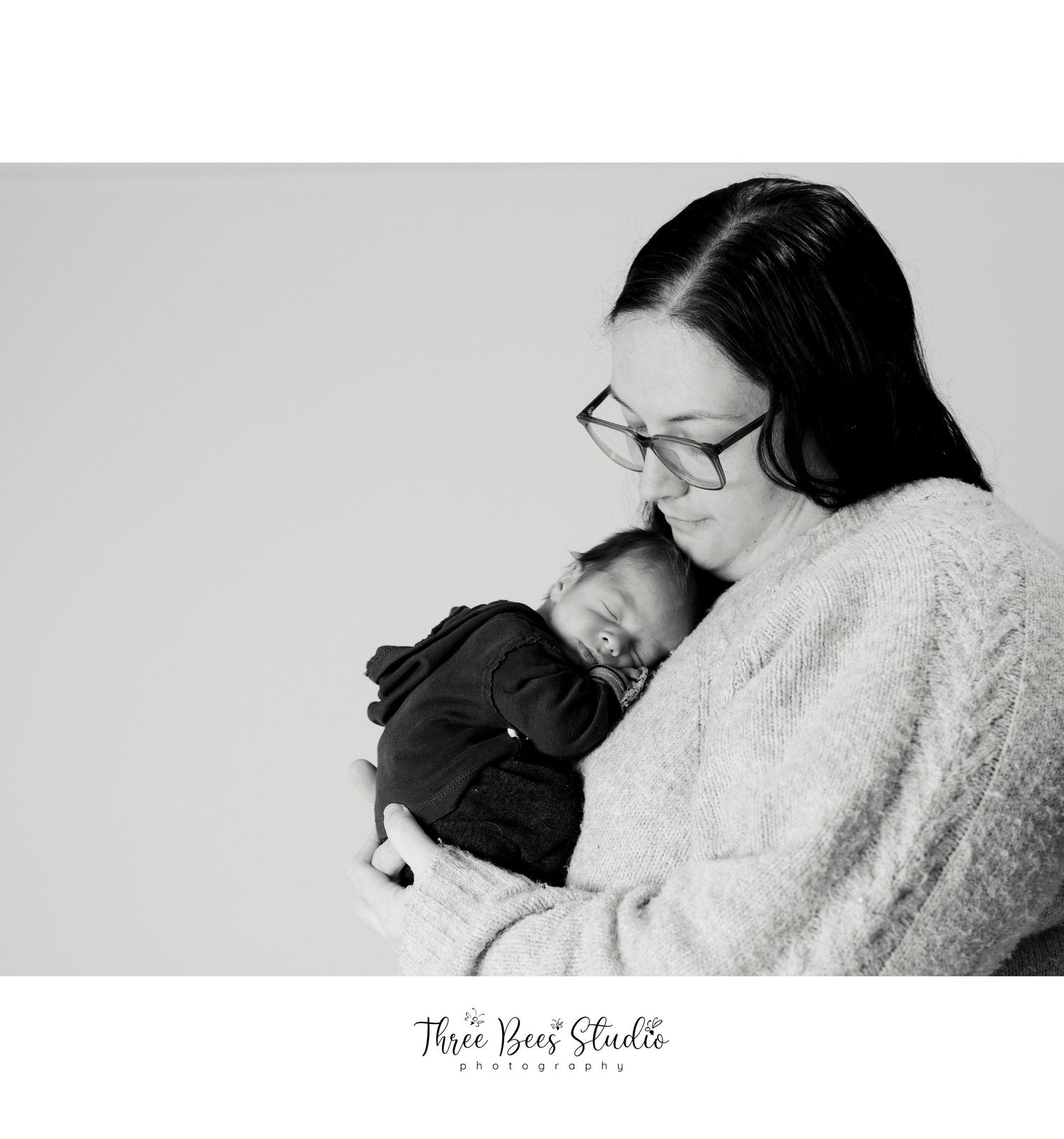 Black and white portrait of mother holding sleeping newborn in cozy sweater.