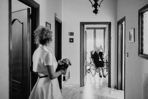 La sposa con il bouquet guarda una persona anziana in corridoio, in bianco e nero.