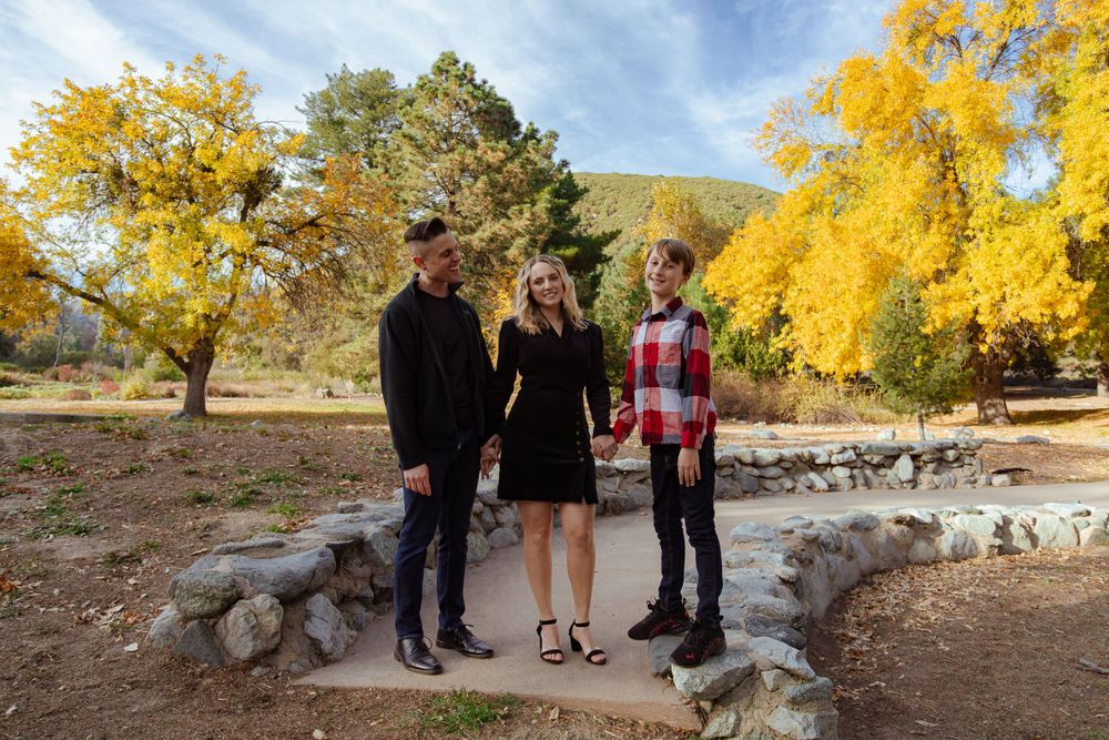 Three people stand together among vibrant yellow fall foliage in a mountain setting.