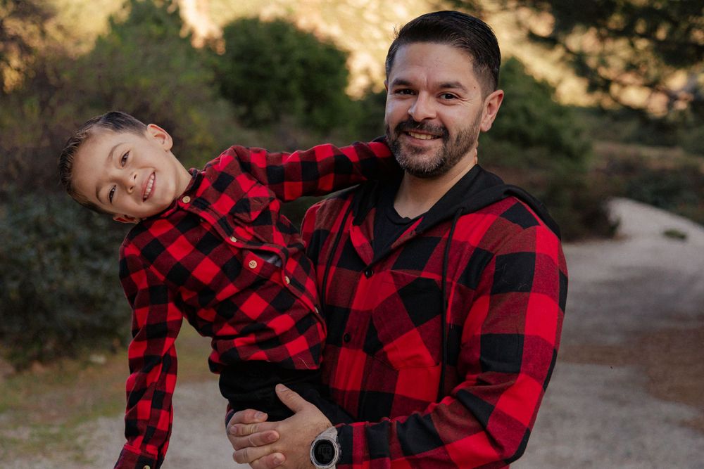 A playful outdoor portrait of two people wearing matching red and black buffalo plaid shirts.