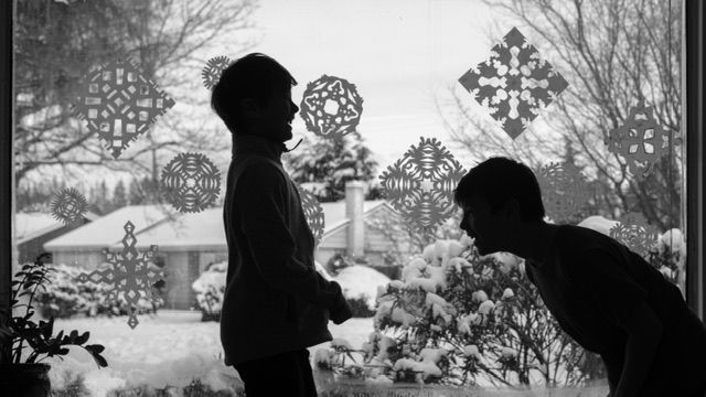 Black and white photo of two laughing children silhouettes in front of snowflake installation, winter, North Vancouver