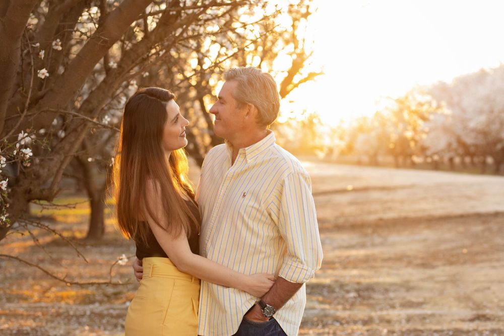 Couple sharing intimate moment among blooming trees at golden hour.