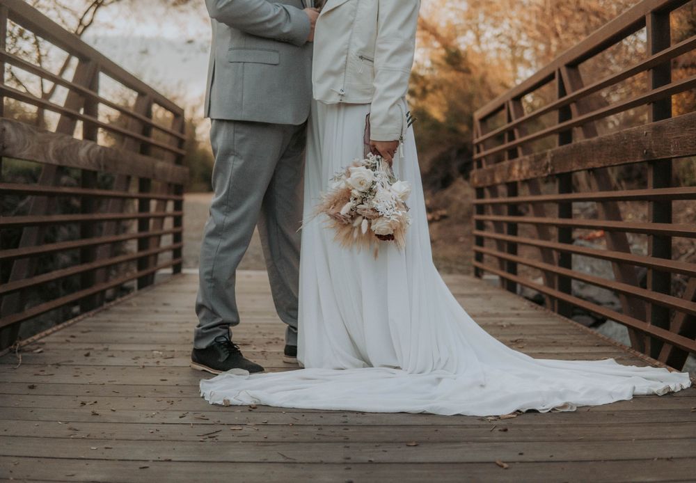 Wedding couple posing on rustic wooden bridge in romantic outdoor setting.