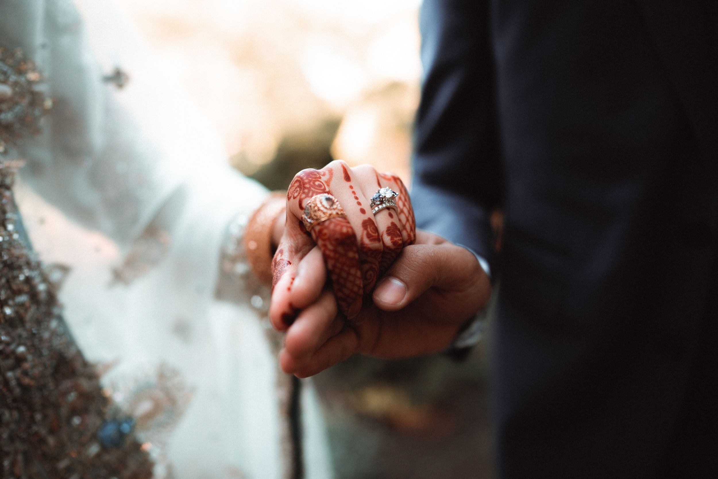 Hands intertwined, a diamond ring gleams beside intricate henna art, symbolizing unity and the promise of forever