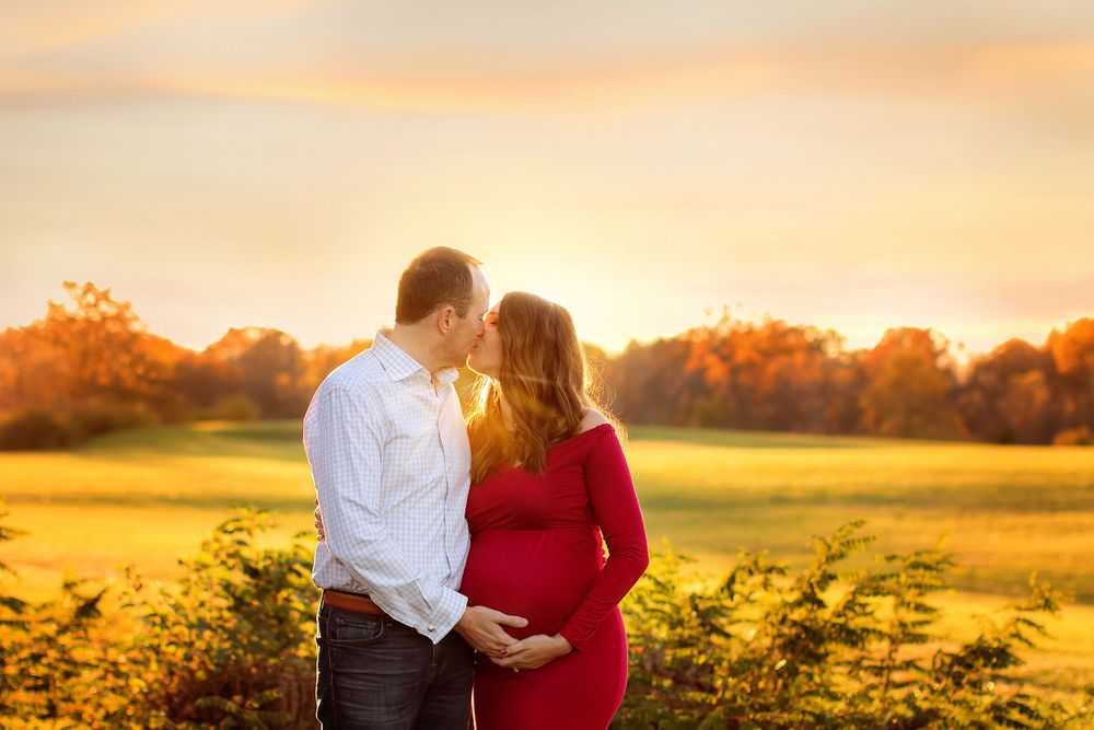 man and pregnant wife kissing in sunset
