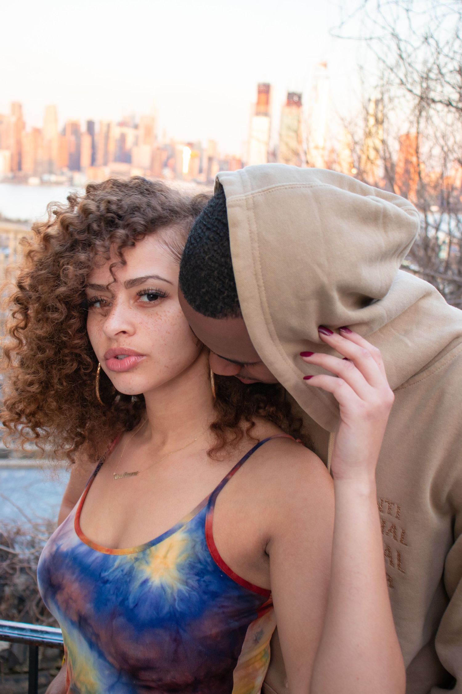 Beautiful couple share an intimate moment against an urban sunset backdrop with NYC buildings visible in the background.