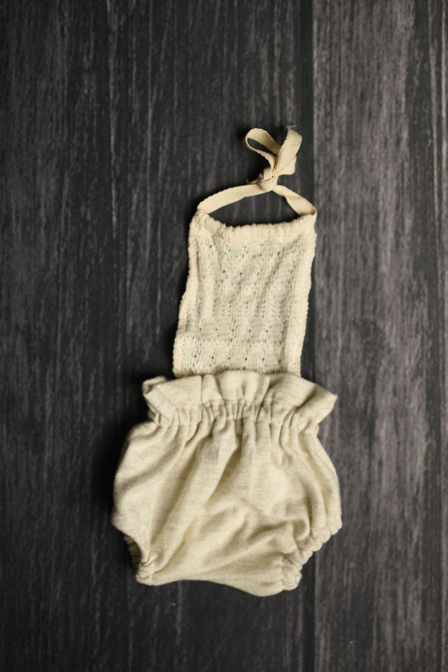 Cream-colored knit baby romper displayed on dark wooden background.