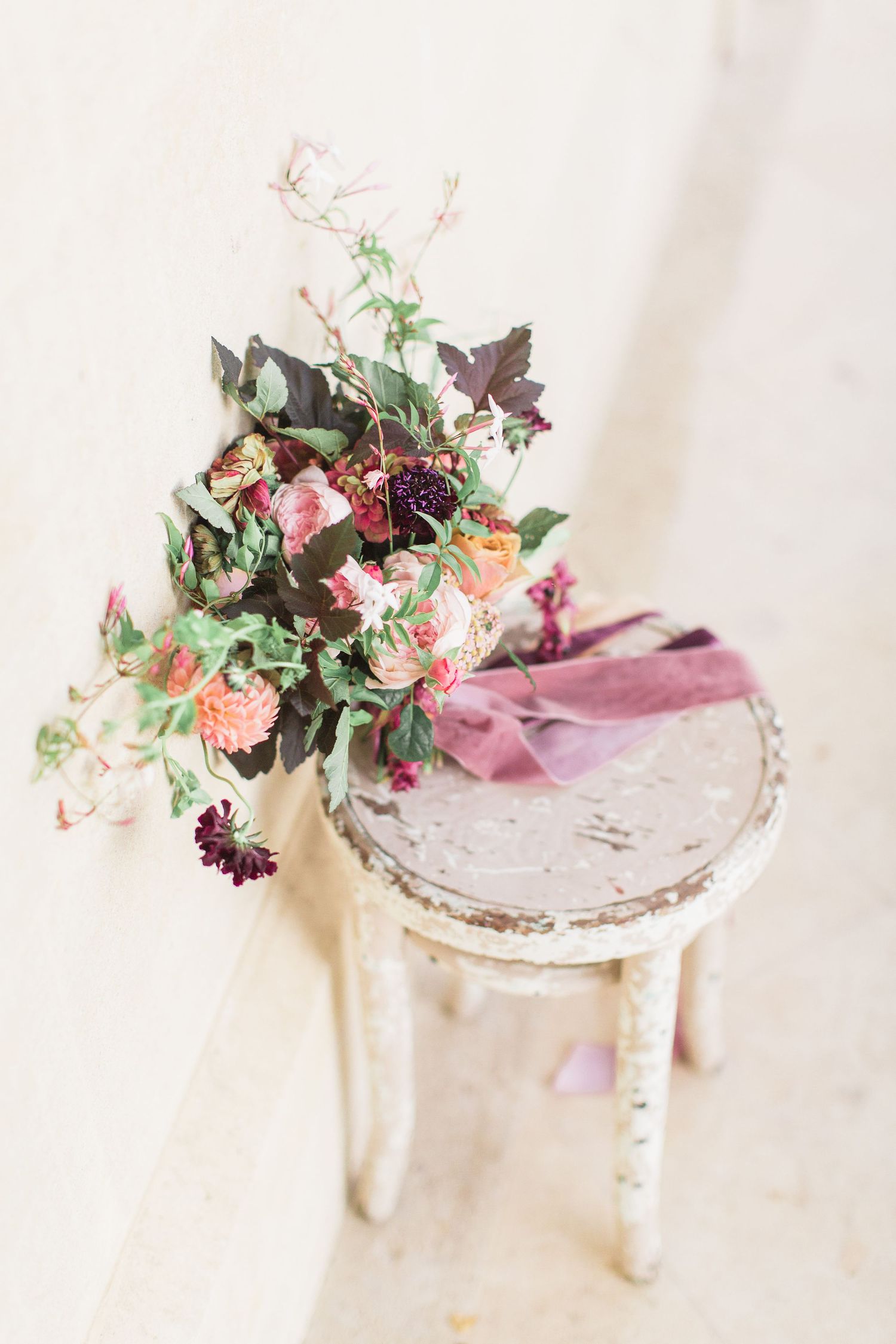 A white rustic stool garnished with delicate floral arrangements in soft peach and burgundy hues against a light background euridge manor