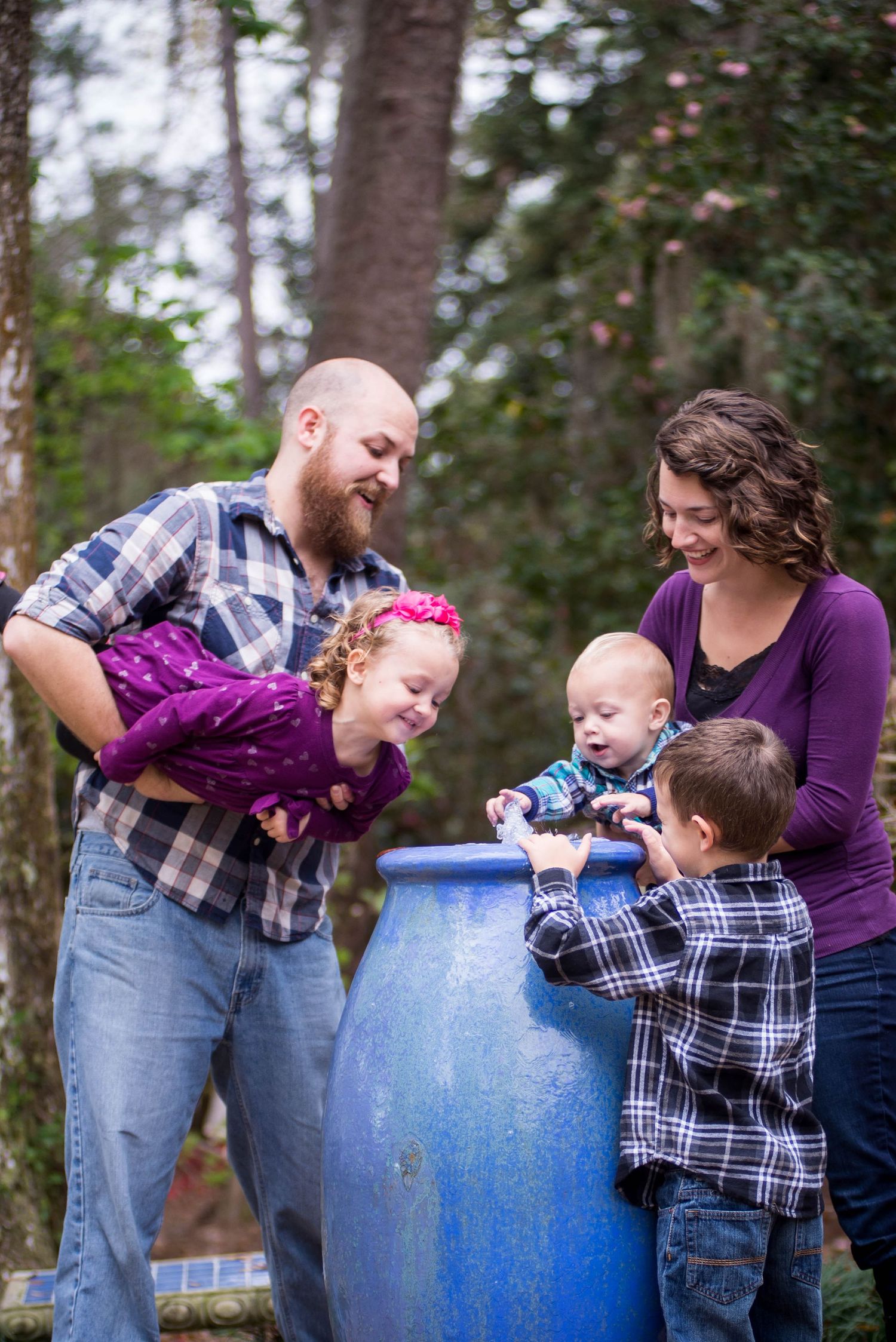 Family gathered around blue rain barrel outdoors in casual clothing.