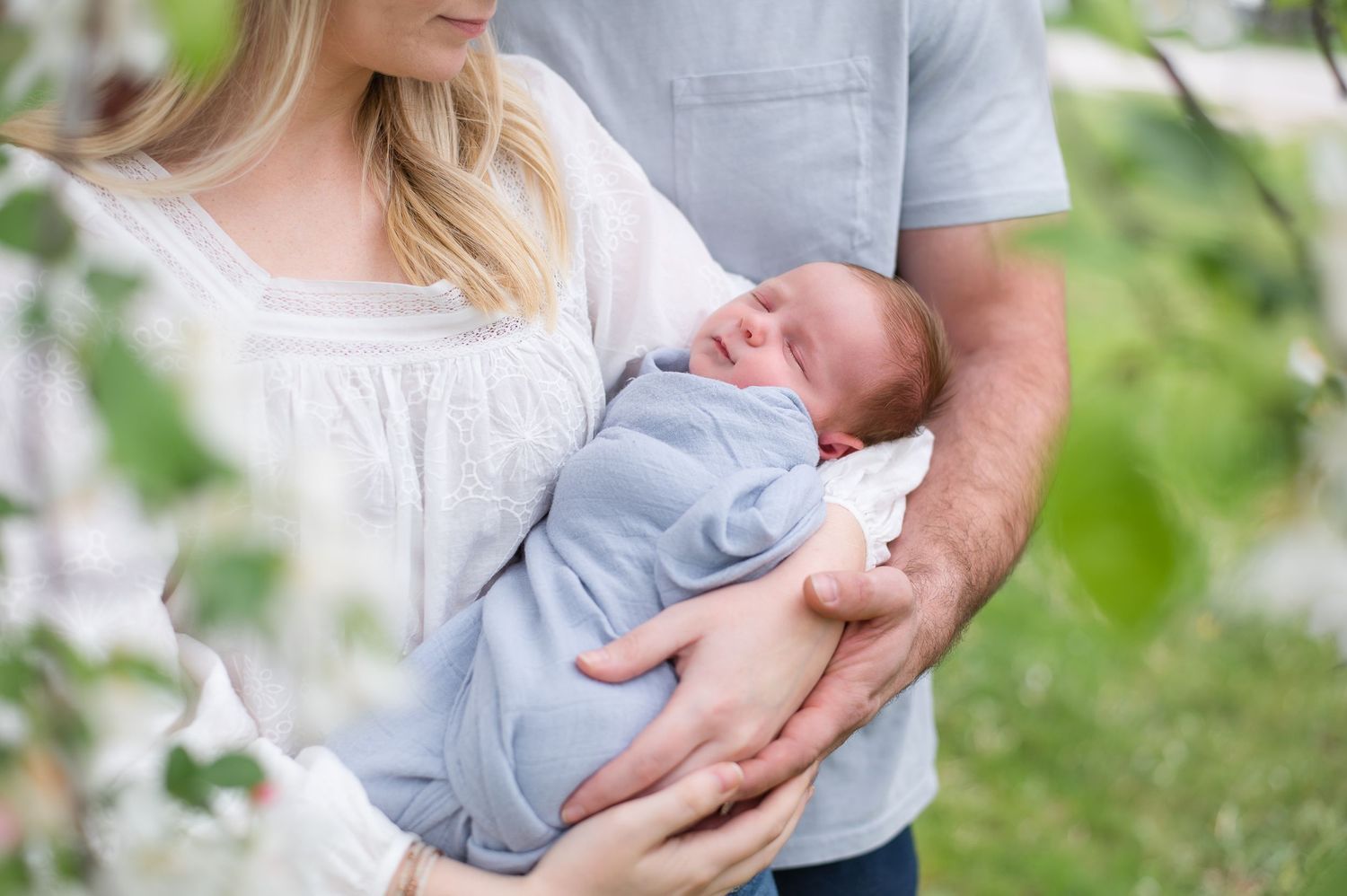 Parents tenderly hold their newborn baby outdoors in natural lighting.