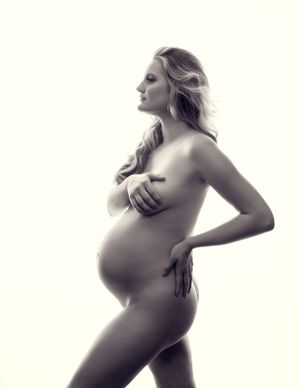 "Expecting mother posing in a studio setting. She's standing confidently, with one hand resting on her hip.