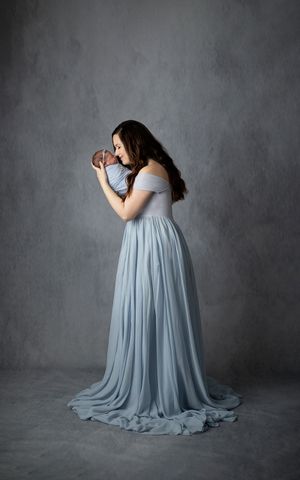 "Expecting mother dressed in a flowing blue gown, posing gracefully in a fine art studio setting.