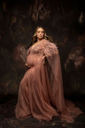 "Elegantly dressed expecting mother posing in a studio setting, holding her baby bump.
