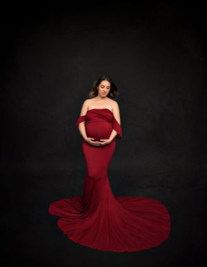 Expecting mother elegantly dressed in a red flowing gown, posing gracefully in a fine art studio.