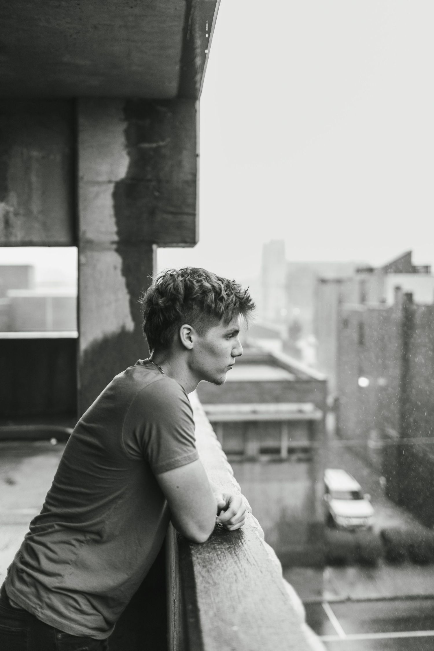 Person leaning against railing on urban rooftop in black and white photograph.