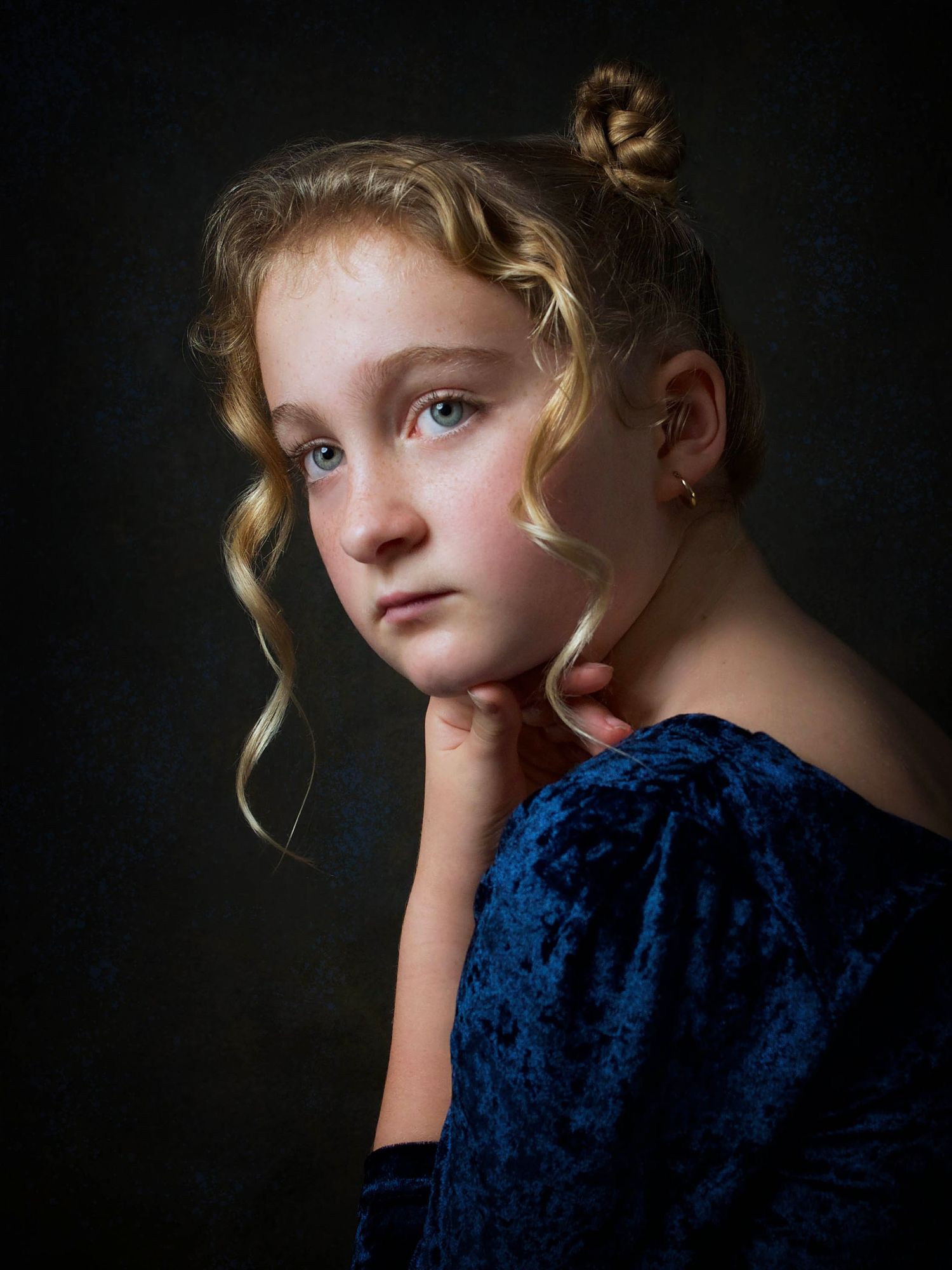 portrait of a young blonde girl with two braided buns and curls wearing a blue velvet dress