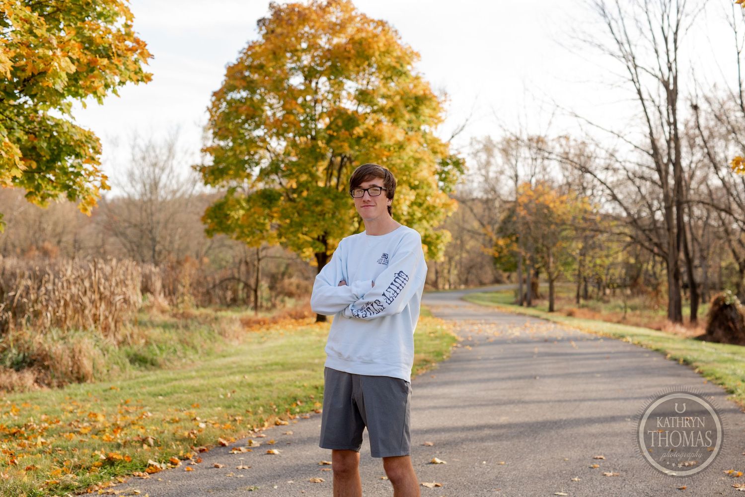 Person in white sweatshirt stands on autumn path with yellow trees in background.
