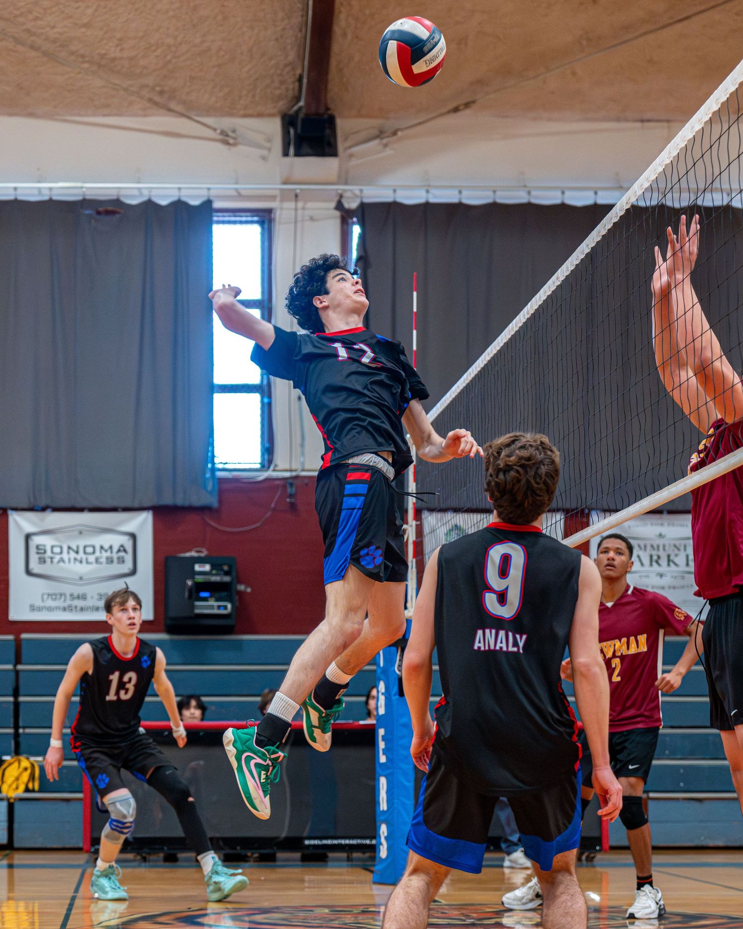 Indoor volleyball player leaping high for spike while opponents prepare to block.
