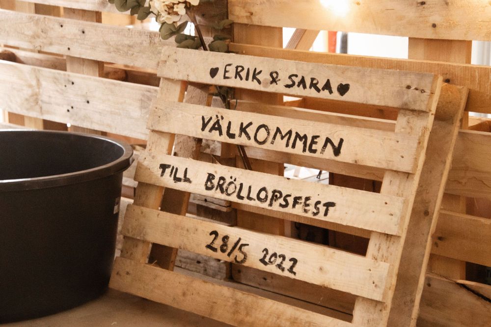 Wooden pallet sign with Swedish text welcoming guests to a celebration.