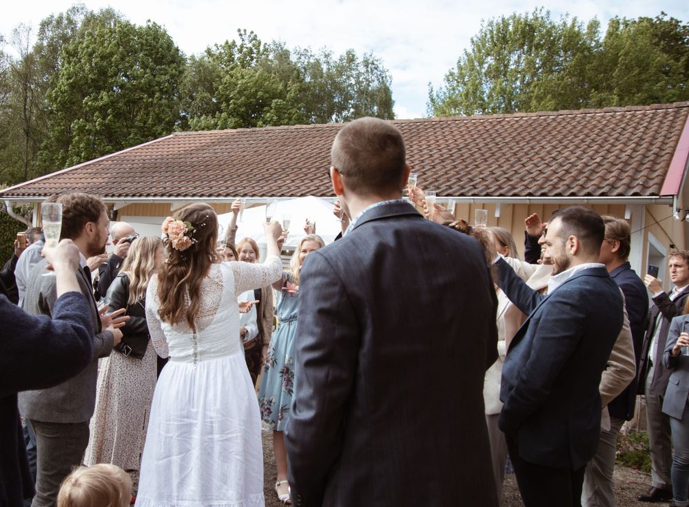 Wedding guests celebrating at an outdoor reception with raised hands under a tiled roof.