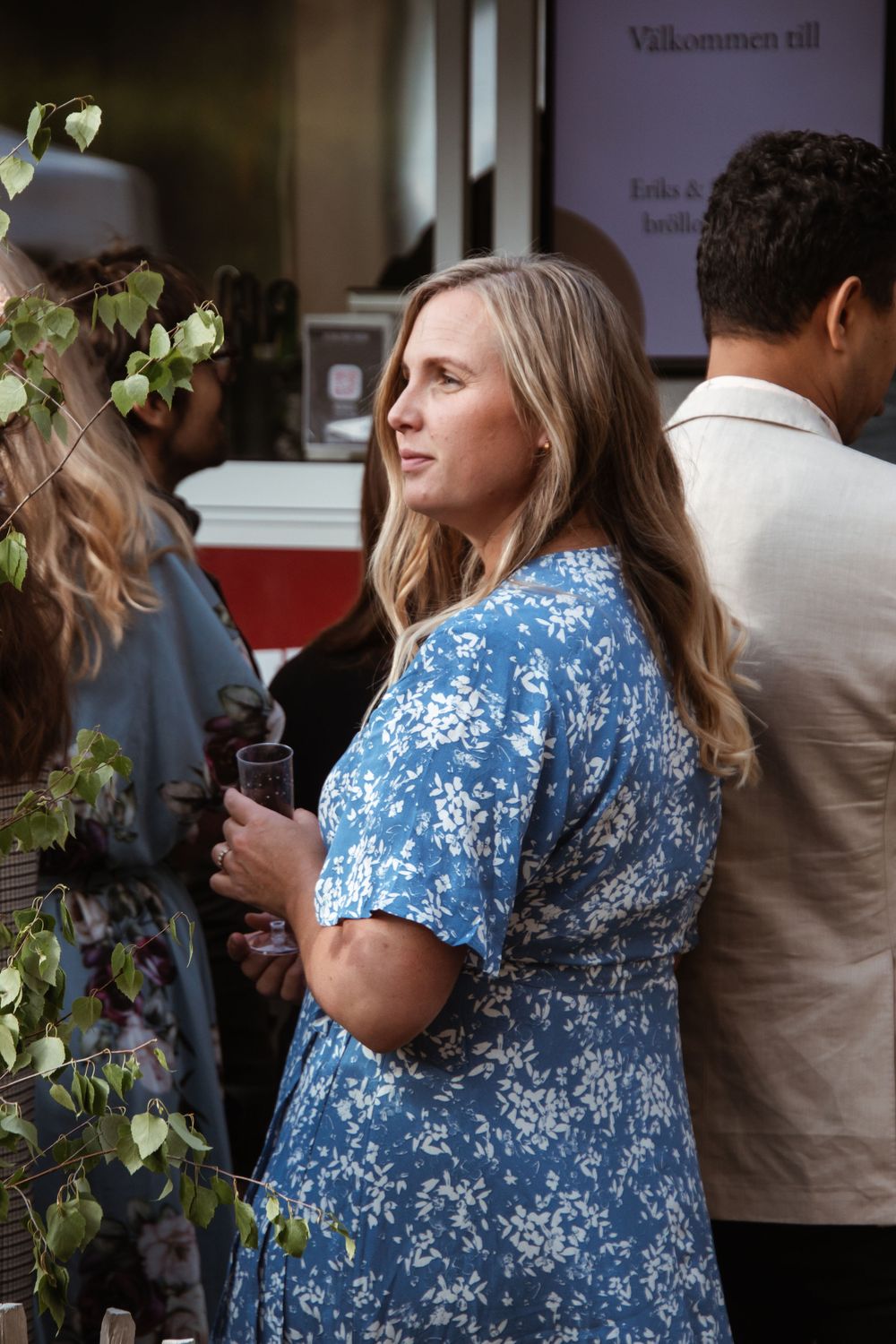 A guest in a blue floral dress mingles at an outdoor wedding reception.