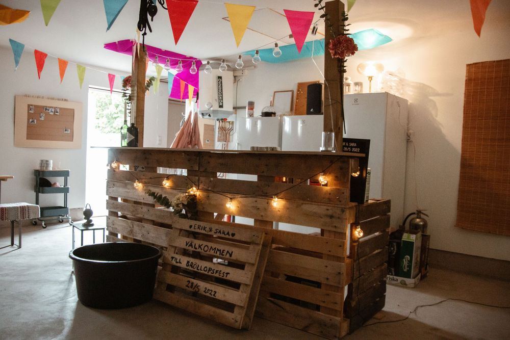 Rustic wooden bar with string lights and colorful bunting flags in an indoor space.