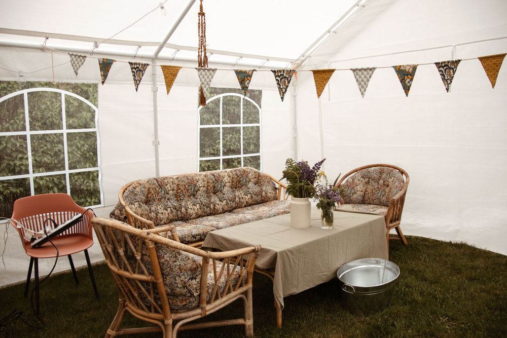Outdoor event setup with wicker furniture and bunting flags in a white tent.