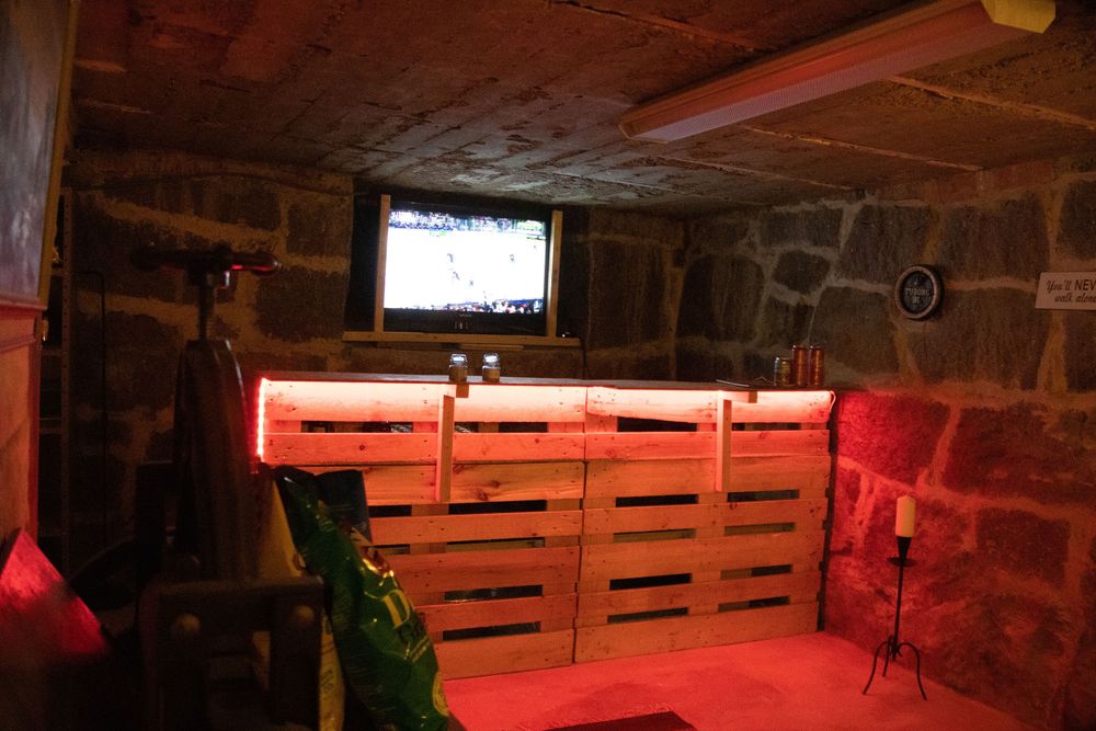 Dimly lit basement bar with red LED lighting and wooden pallet decor creates a cozy atmosphere.