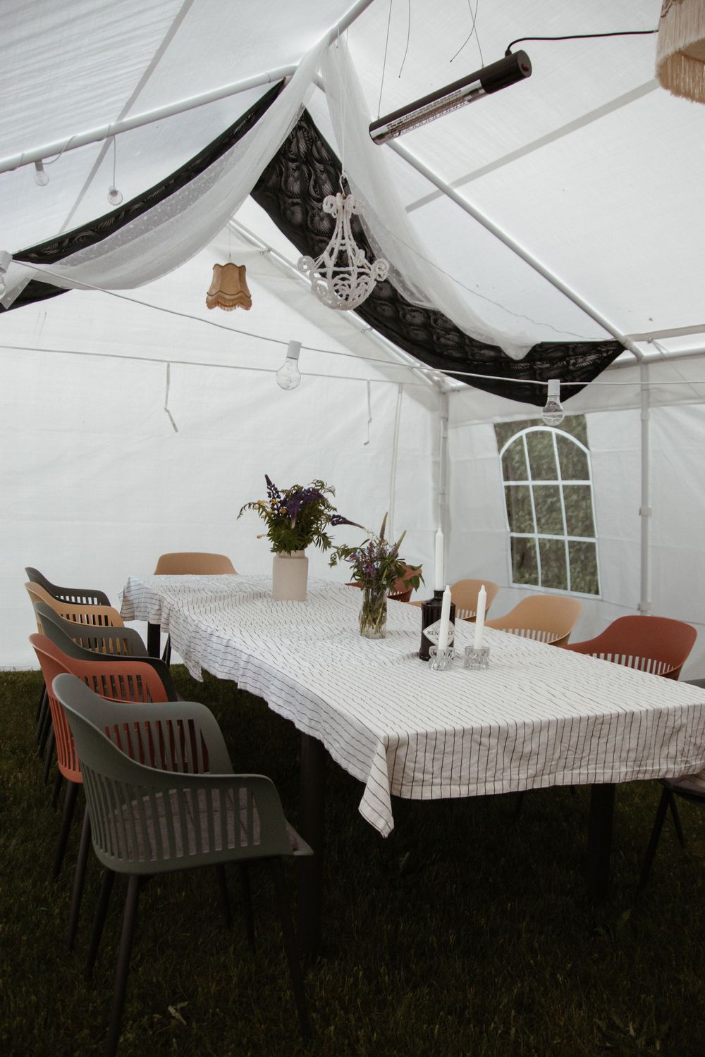 White tent reception setup with a long table decorated with simple floral centerpieces and plastic chairs.