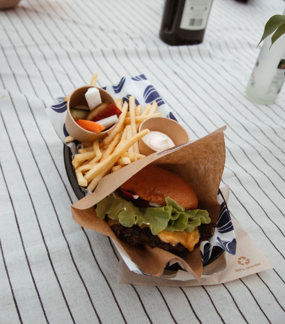 A cheeseburger and french fries served in paper wrapping on a striped surface.