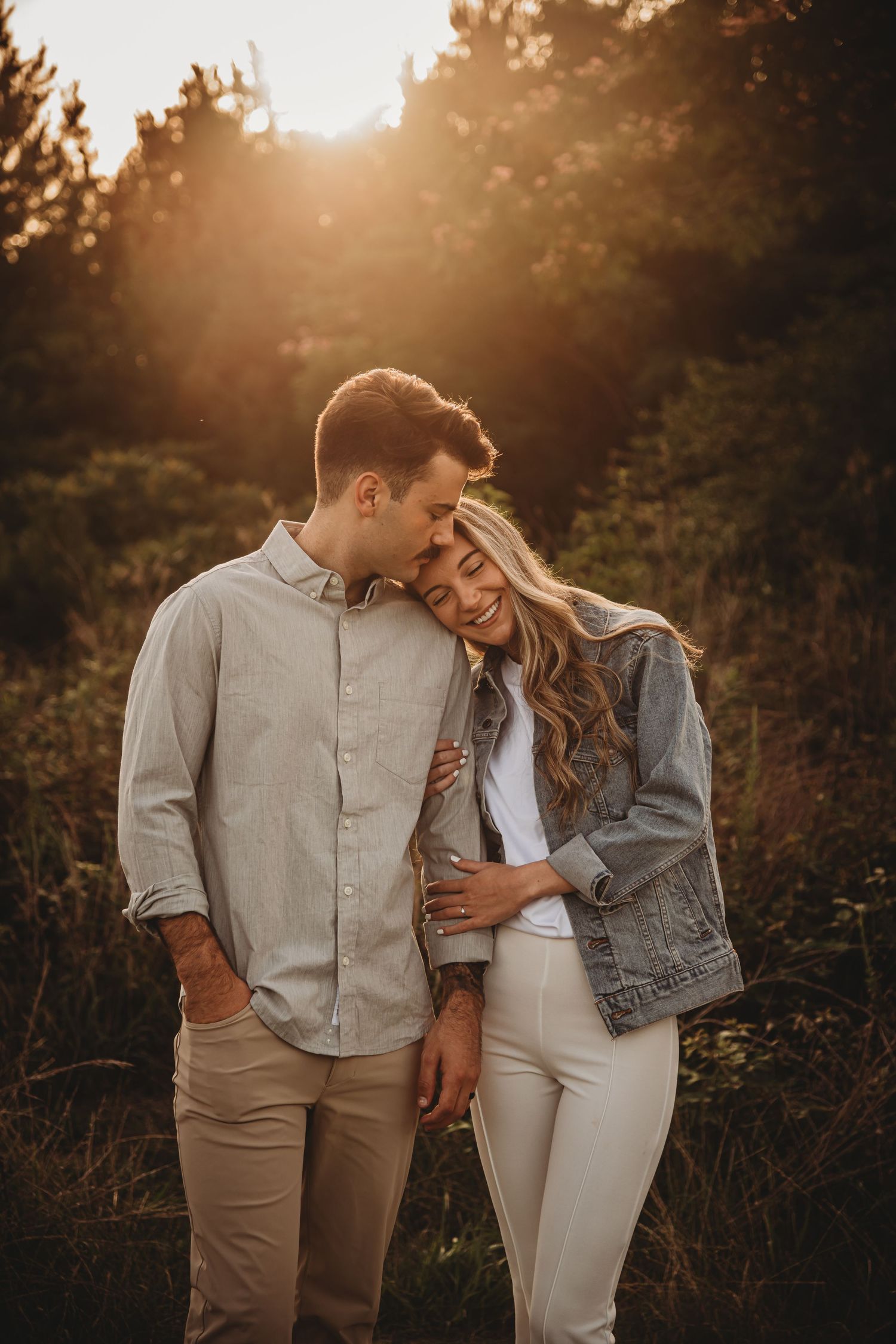 Romantic sunset photoshoot with couple in casual attire among trees.