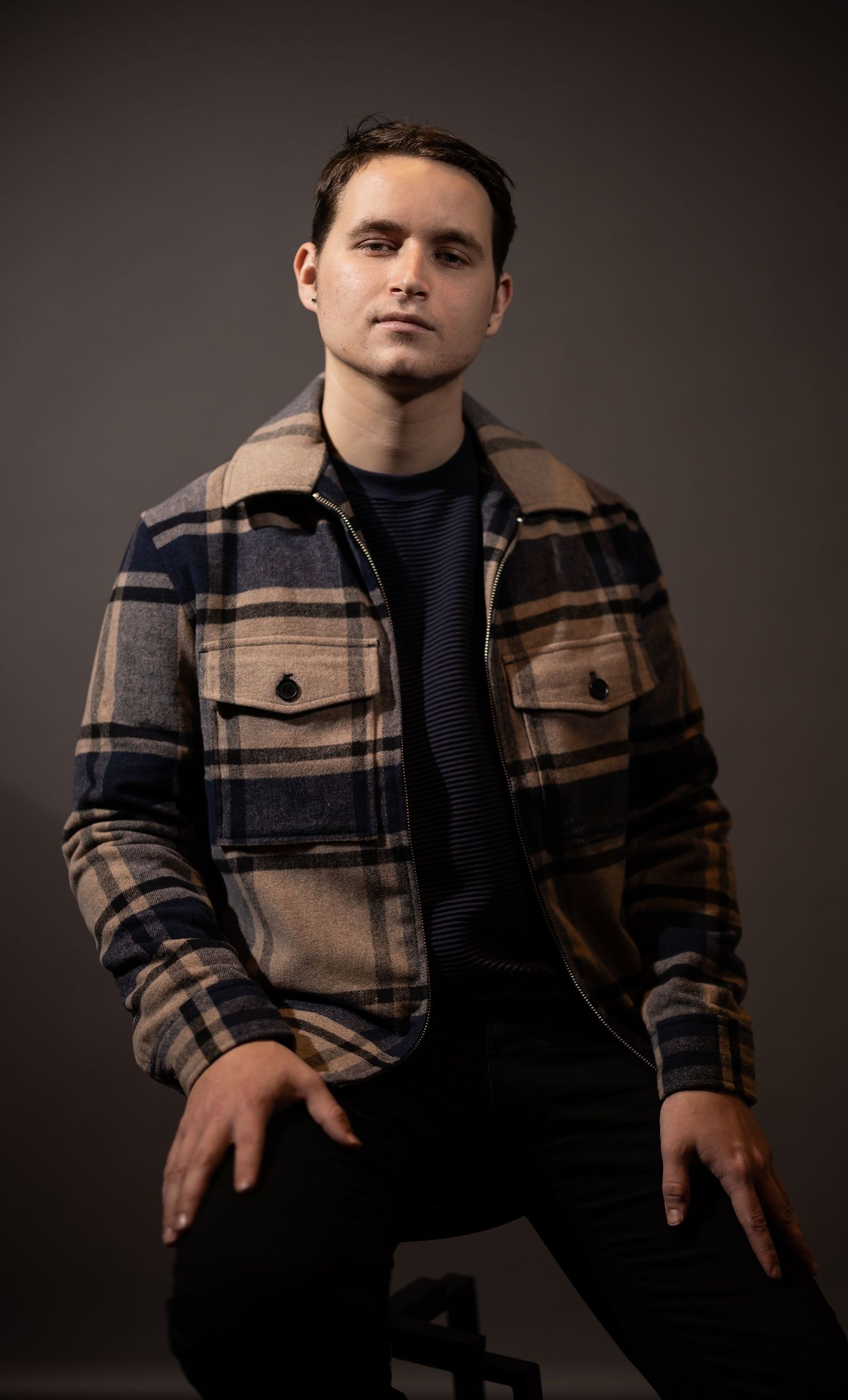 Portrait of someone wearing a plaid flannel jacket and dark shirt against a dark background.