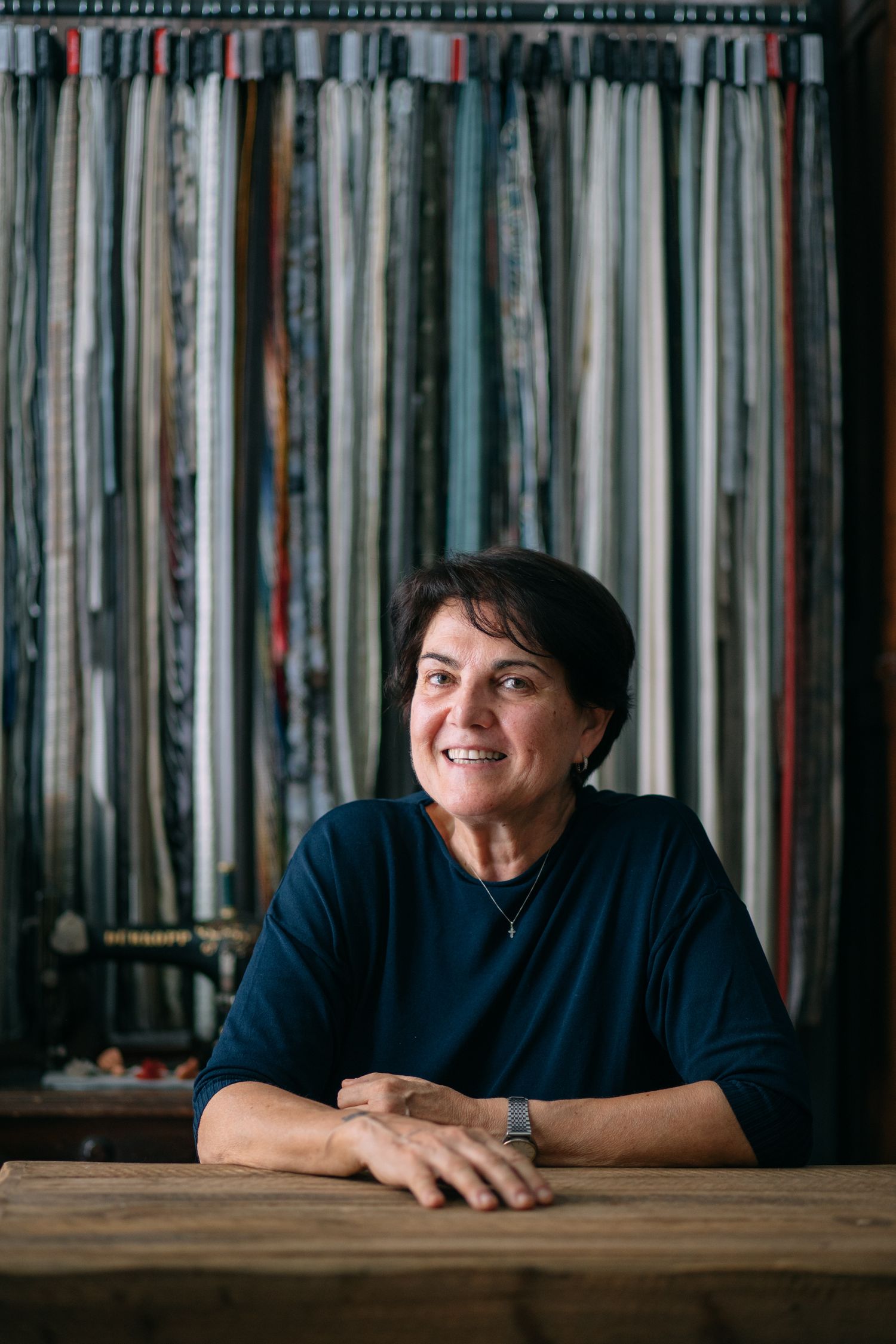Portrait of a person seated at wooden table with hanging fabric backdrop.