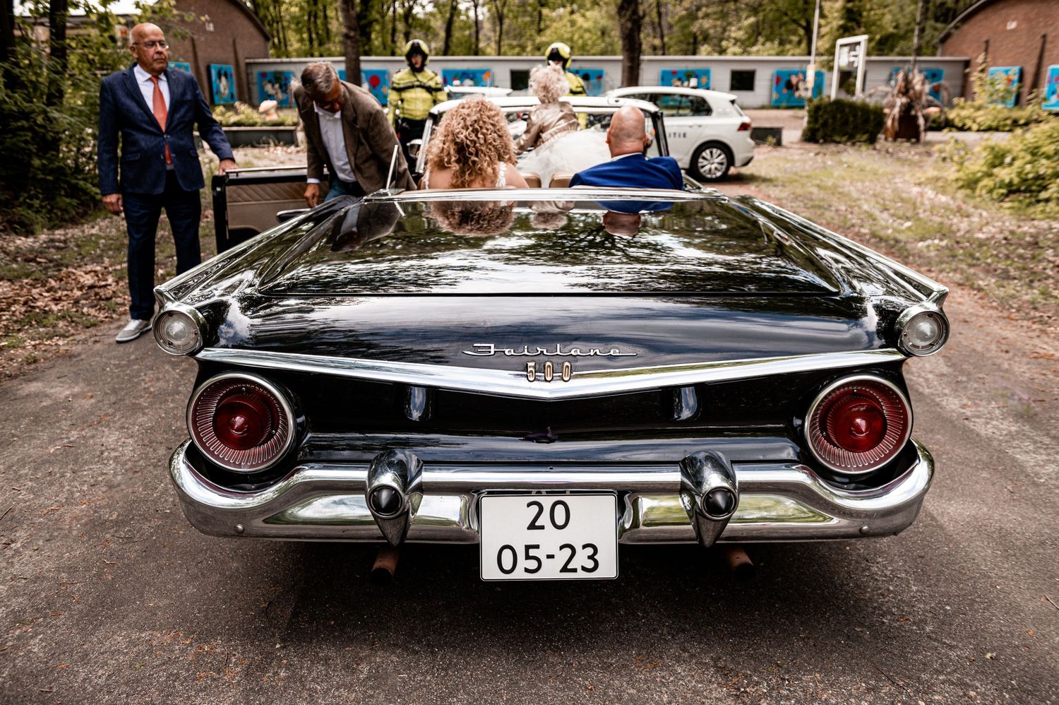 Classic vintage black car with chrome details parked at outdoor wedding venue.