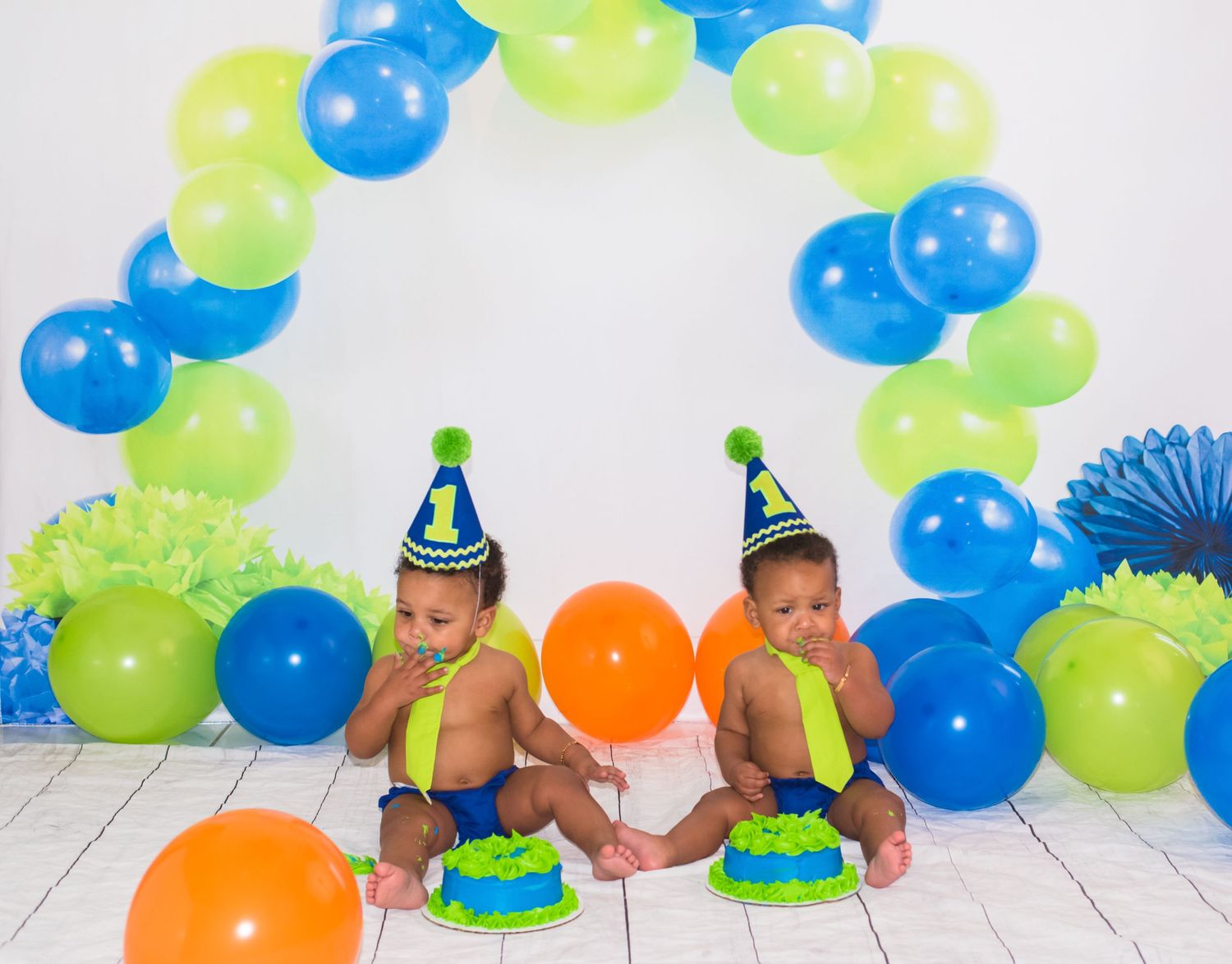Birthday celebration setup with blue and green balloon arch and party hats.